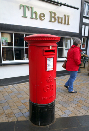 Bracknell, England - February 20, 2018: A pedestrian passes by a traditional red, King George post box in front of The Bull public house in Bracknell, Englandのeditorial素材