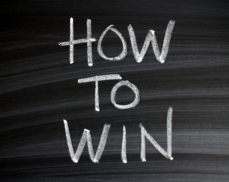 The words How To Win written by hand in white chalk on a wiped blackboardの写真素材