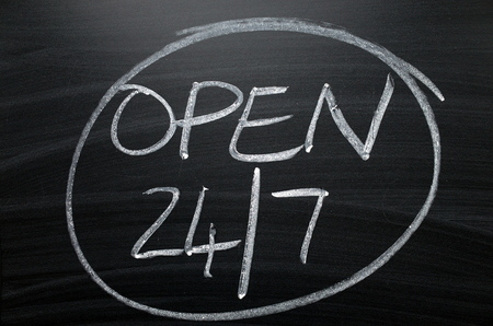 Open twenty four hours by seven written by hand in white chalk on a blackboard signの写真素材