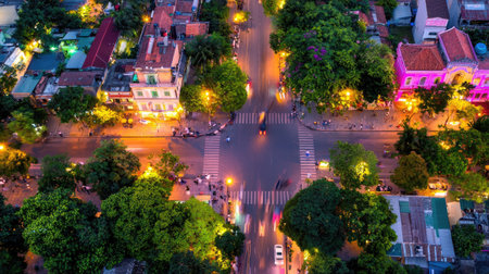 This captivating aerial view showcases an urban intersection at night, illuminated by colorful city lights and surrounded by lush trees, creating a vibrant atmosphere.の素材