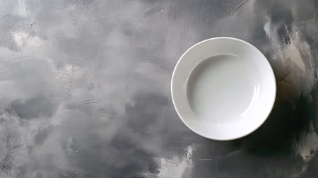 A minimalist composition featuring an empty white bowl on a textured gray background. Ideal for showcasing culinary concepts or plating ideas.の素材