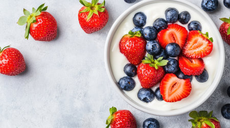 A vibrant bowl of fresh strawberries and blueberries sits atop creamy yogurt, creating a healthy and delicious breakfast option. The light background enhances the colorful fruits, making it visually appealing.の素材