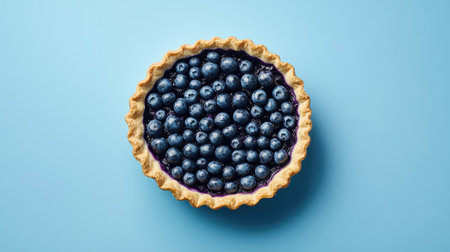 A fresh blueberry pie featuring a golden crust filled with plump blueberries sits on a soft blue background, showcasing its vibrant colors and delicious appeal.の素材
