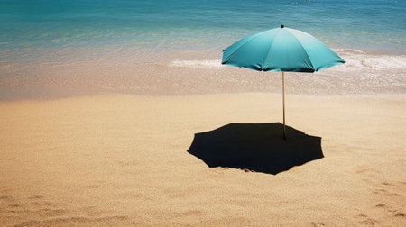 Empty beach umbrella casting a shadow on the sand, with space for copyの素材