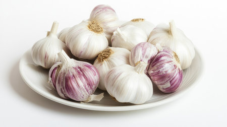 Top view of garlic cloves and bulbs arranged on a white plate with a clean white background, leaving ample copy spaceの素材