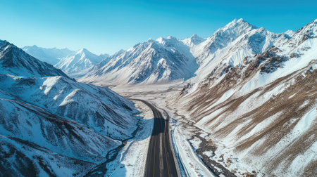 Top view of a road through high-altitude mountains with snow-covered peaks and clear skies. Ideal for winter travel contentの素材