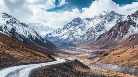 Scenic view of a winding road through high-altitude mountains with snowy peaks and expansive valleys. Ideal for adventure themesの素材