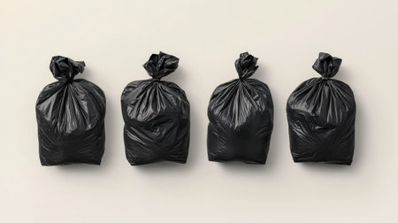 This image features four black garbage bags tied securely and lined up against a light surface. Ideal for themes of cleanliness, waste management, and home organization.の素材
