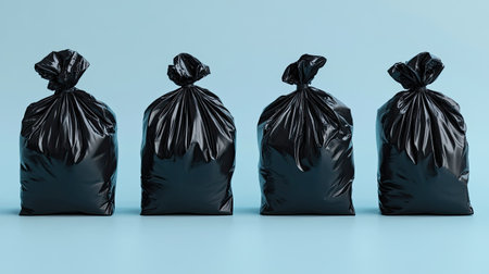 Four black garbage bags arranged on a blue surface symbolize waste management and environmental responsibility. Ideal for concepts related to cleanliness and disposal.の素材