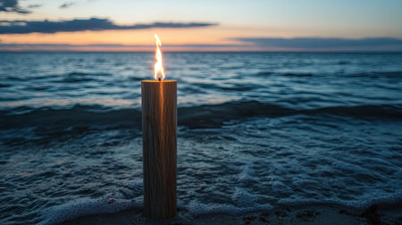 A tranquil beach scene featuring a lit candle standing on the shore as waves gently roll in, creating a serene atmosphere during sunset.の素材