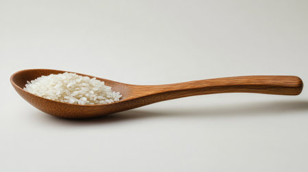 A beautiful wooden spoon filled with raw white rice, set against a soft neutral background. This image highlights the simplicity and nutritious aspect of rice as a key kitchen ingredient.の素材