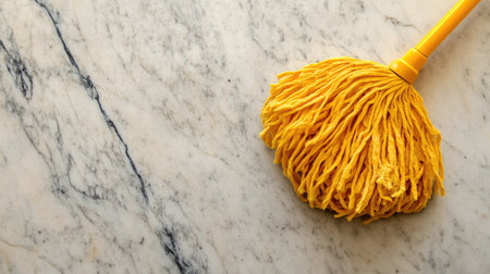 A bright yellow mop head rests on a clean, polished marble surface, symbolizing effective cleaning tools for maintaining household hygiene. Ideal for stock images.の素材
