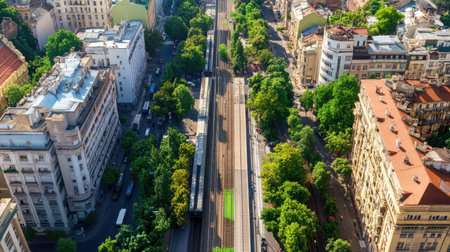 This aerial view captures an urban train station nestled within a vibrant city landscape. Lush greenery contrasts with the city's architecture, showcasing a blend of nature and infrastructure.の素材