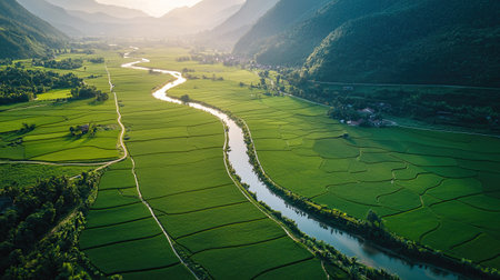 This breathtaking aerial view showcases a lush green valley with a gentle river winding through, framed by majestic mountains under bright sunlight. Perfect for nature lovers.の素材