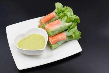 Vegetable salad with crab sticks arranged in a white plate on a black background