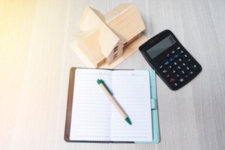 Wooden house model and calculator, note book and pen on wood floor on finance and business banking conceptsの写真素材