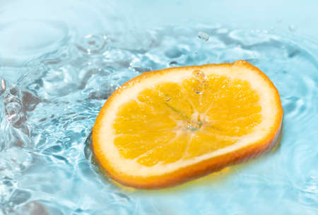orange skin falling into water splash on blue background and healthyの写真素材