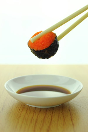holding shrimp eggs sushi roll with chopsticks and shoyu sauceの写真素材