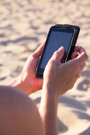 Mobile phone in hands on the beachの写真素材