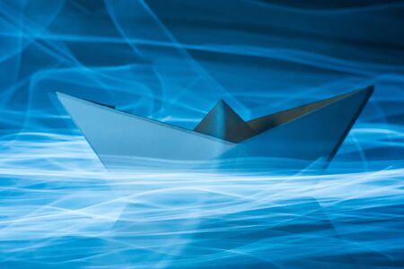 Paper boat splitting blue light trails symbolizing waves and energy efficiency