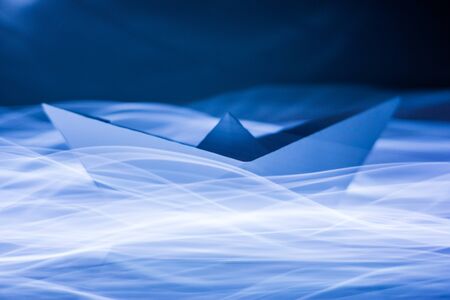 Paper boat splitting blue light trails symbolizing waves and energy efficiencyの写真素材