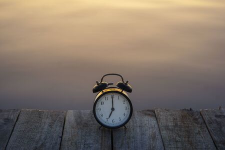 Summer time concept. Alarm clock on wooden bridge on sea sunrise background