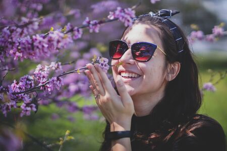 Beautiful caucasian woman with glasses smiling under spring blossoming cherry trees. Concept: Happy people and freedomの写真素材