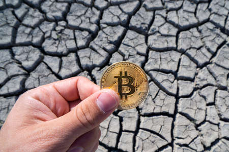 BITCOIN OVER DRY LAND IN HAND SYMBOLIZING GLOBAL WARMING AND CRYPTO MININGの写真素材