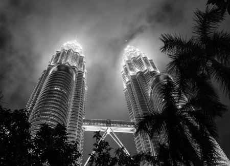 Black and white picture of the Petronas Towers on a misty night. Taken at ground level shot through...