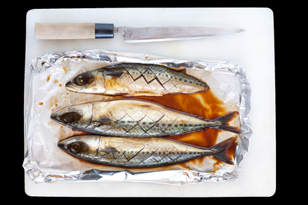 Blue mackerel in aluminium foil on cutting board with japanese chef knifeの写真素材