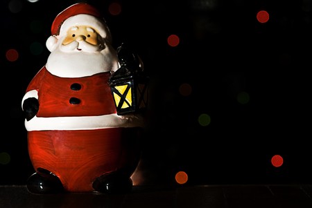 A christmas ornament of Santa holding a lantern. Lights on a christmas tree are in the background.の写真素材
