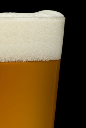 A close up of a glass of beer on a black background. Beer is a lovely golden colour with white...