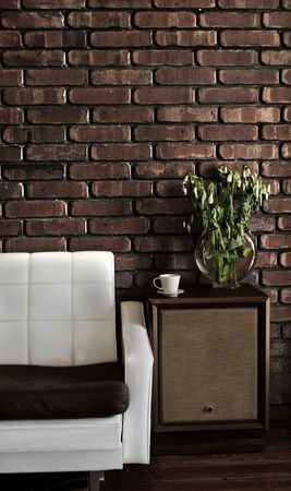 Retro styled lounge room showing a couch, speakers, cup, plant on wooden floor and a brick wall.の写真素材