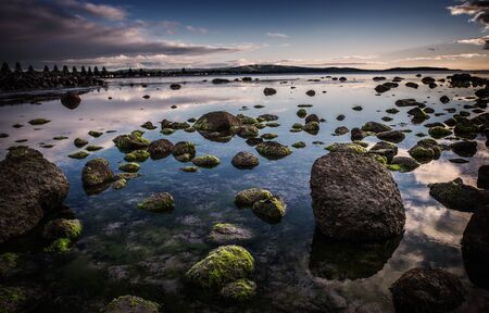 Moss covered rocks at sunrise  The water is still allowing both reflections of the sky and being...