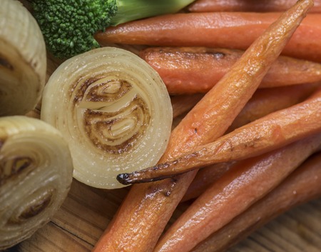 Perfectly roasted carrots and onions on a wooden platterの写真素材