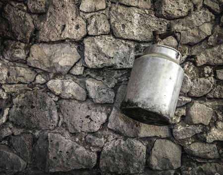 An old fashioned milk tin hanging from an ancient stone wallの写真素材