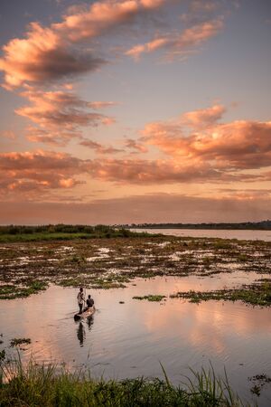 Two men out in a traditional canoe fishing at sunset in Africaの写真素材