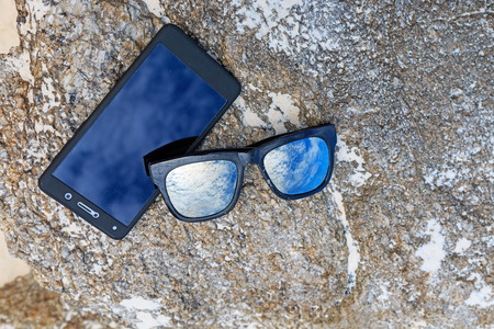 Sunglasses with mobile on stone in beach.の写真素材
