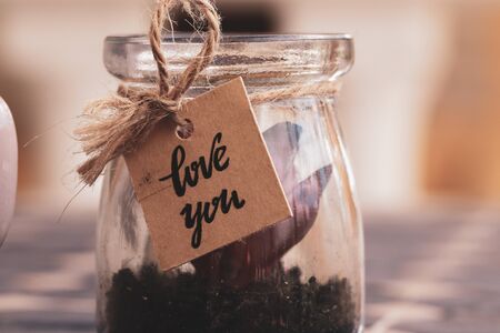 Vintage style photo of a romantic scene featuring an old rope, a cardboard sign and a plant inside a glass with the light going through it.の写真素材