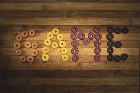 This scene features donut shaped cereals orange, yellow, purple and pink spelling the word Game in...