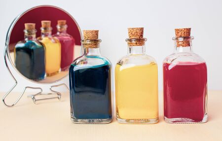 Three glass bottle with blue yellow and red liquid with reflection in a round mirror: the table made of wood and the background is white. The small bottle have cork leads.の写真素材