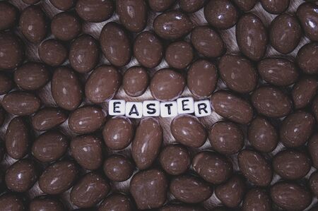 Chocolate peanuts eggs with the word Easter in white and black plastic square letters. Background texture made of the shapes of the chocolate eggs with the light focused on the word easter.の写真素材