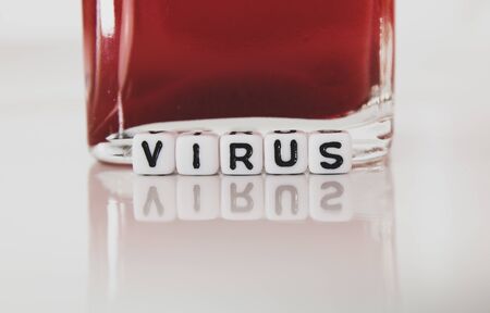 Virus white square plastic letters macro on reflective plate with red liquid in container. Macro photography.の写真素材