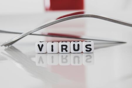 Virus work in white plastic letters on plate with form and red bottle in the background. Macro conceptual photography.の写真素材