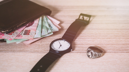 Plastic Watch, Silver ring and Thai money in Brown Wallet on the desk.