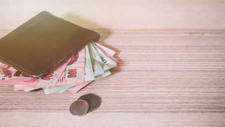 Thai money in the Brown wallet and Silver coin on wooden desk.