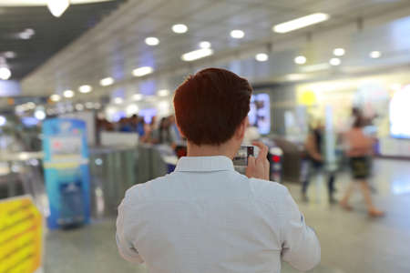Man taking a photo of people walking in subway station with smartphone