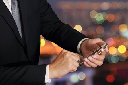 businessman hand hold and touch screen smart phone, cellphone on abstract blurred bokeh of city night light backgroundの写真素材