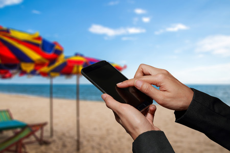 Woman hand hold and touch screen smart phone, cellphone  on blurred abstract beach background as communication and travel concept.の写真素材