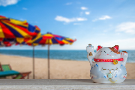 Lucky cat piggy bank with blurred abstract beach under blue sky background, abstract background to time to start to saving or lucky for keep money concept.の写真素材